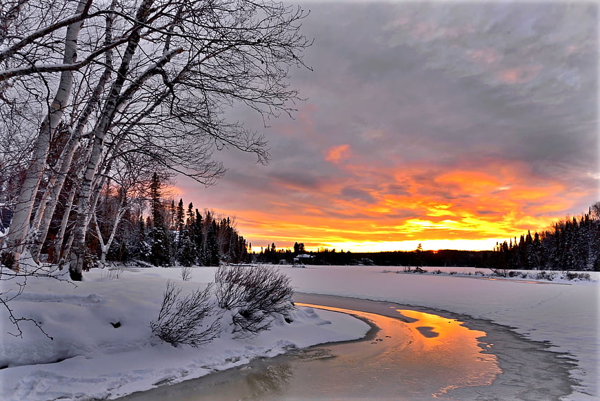 Winter sunset over a frozen river with birch trees and snow