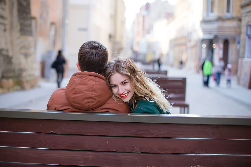 Happy couple on city bench, woman smiling over shoulder
