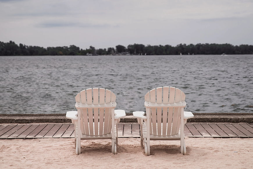 Two White Adirondack Chairs on Sandy Lake Shore