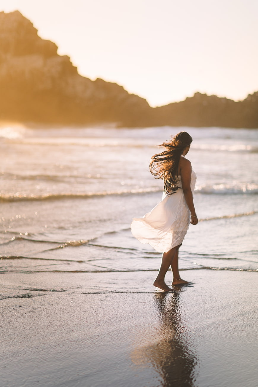 Woman in White Dress Walking on Beach at Sunset