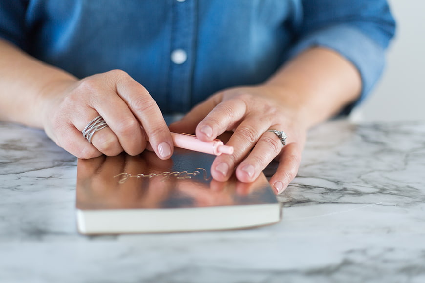 Woman Writing in Rose Gold Notebook on Marble Desk