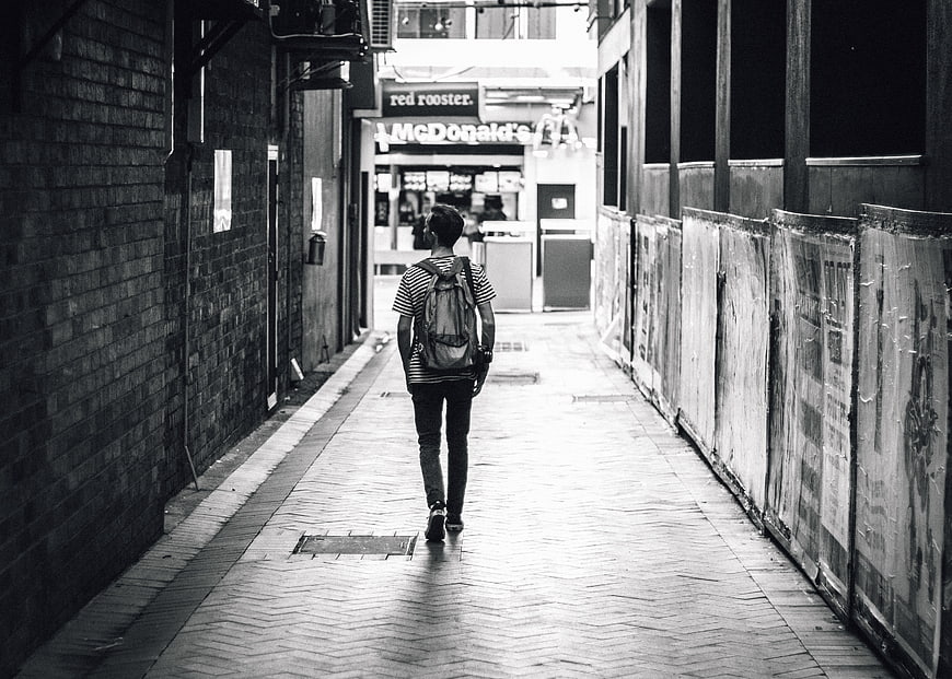 Man with Backpack Walking Down Urban Alleyway