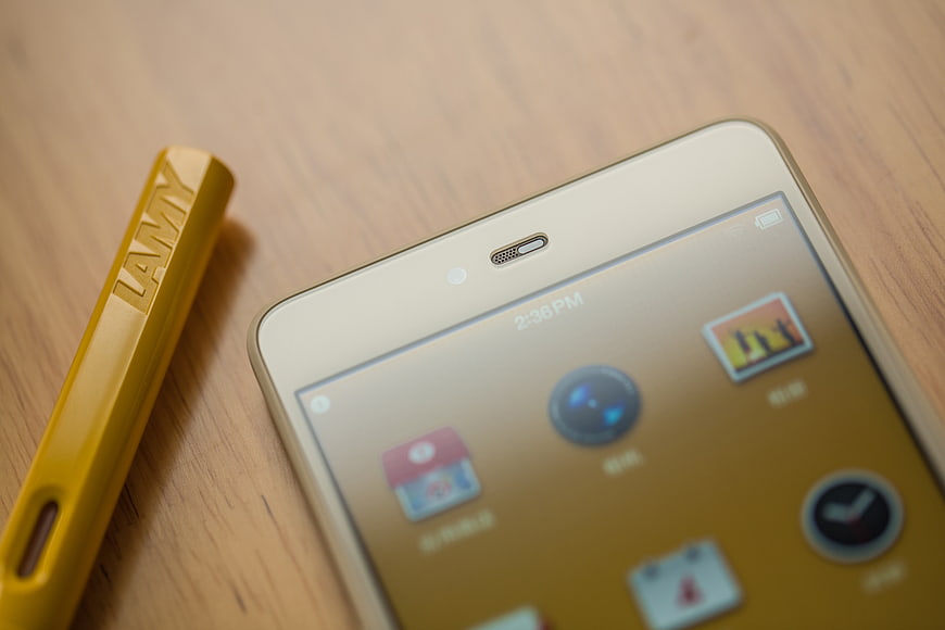 Gold smartphone and yellow Lamy pen cap on wooden desk