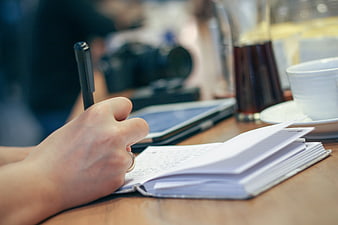 Hand Writing in Notebook at Coffee Shop Desk