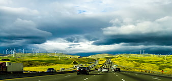 Highway Traffic Through Green Hills With Wind Turbines Under Dramatic Stormy Sky