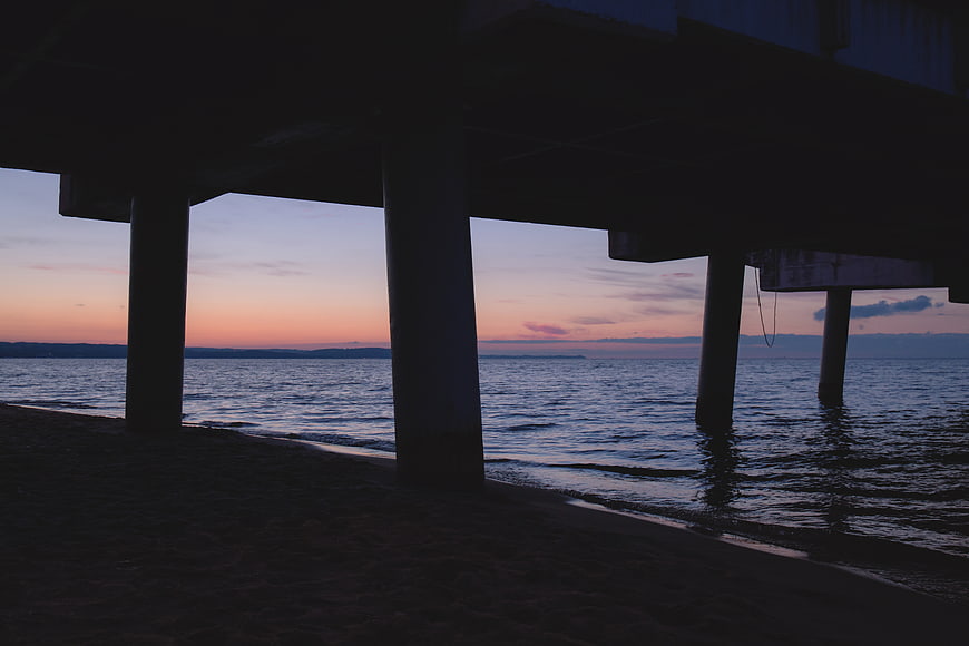 Silhouette of pier pillars at sunset over calm ocean