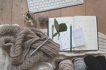 Flat lay of knitting supplies, notebook, and keyboard on wooden desk