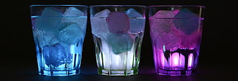 Three illuminated glasses with ice and carbonated drinks on black background