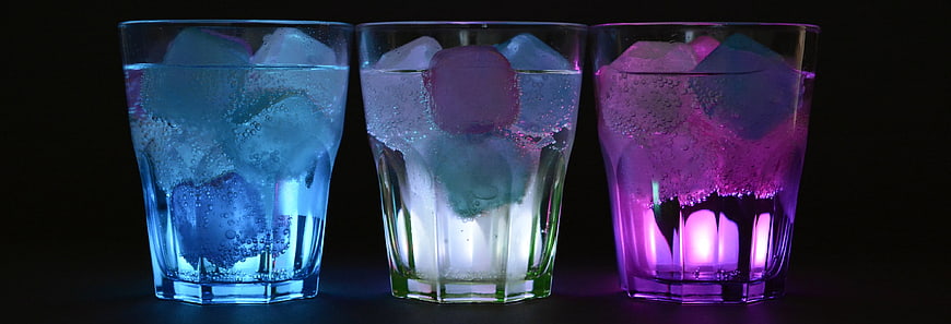 Three illuminated glasses with ice and carbonated drinks on black background