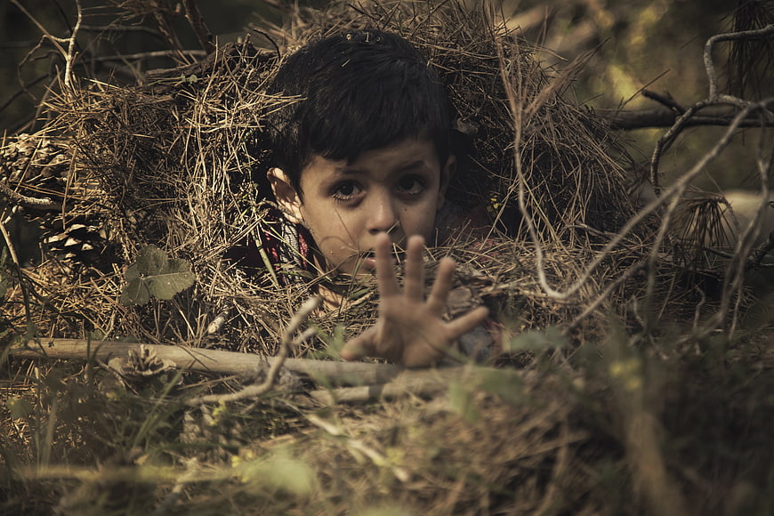 Scared child hiding in forest with hand reaching out