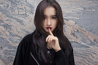 Young Asian woman portrait with finger on lips against textured stone wall