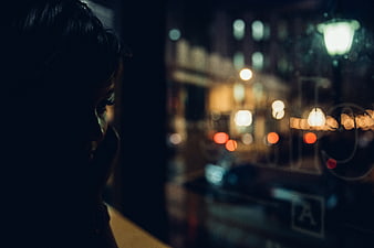 Woman looking out window at night city bokeh lights