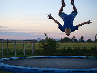 Boy doing backflip on trampoline at sunset