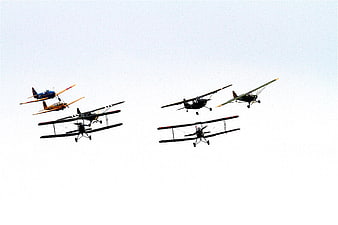 Vintage biplanes flying in formation against a white sky
