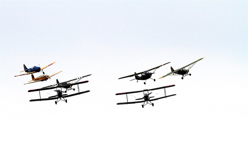 Vintage biplanes flying in formation against a white sky