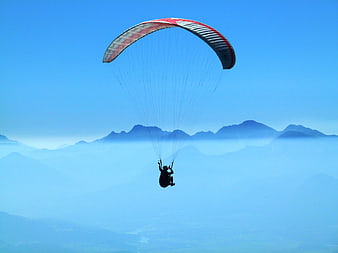 Paraglider soaring above misty mountain layers