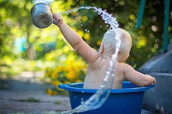 Toddler splashing water from metal cup in blue bucket outdoors