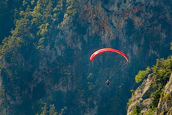 Red Paraglider Soaring Against Rocky Mountain Cliff