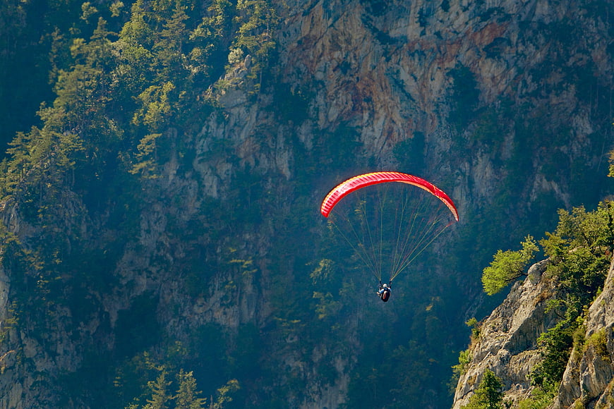 Red Paraglider Soaring Against Rocky Mountain Cliff