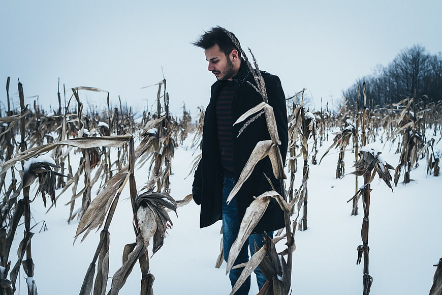 Man in black coat walking through snowy cornfield