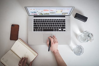 Top-down view of workspace with laptop, notebook, and hands