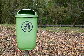 Green outdoor trash bin in autumn park setting