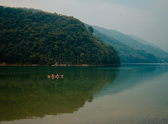 Couple in small boat on calm lake with forested mountains