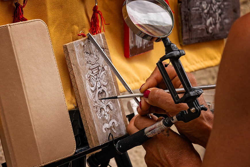 Close-up of hands carving intricate wood art with magnifying glass