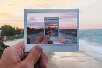 Hand holding polaroid photo of beach sunset cityscape