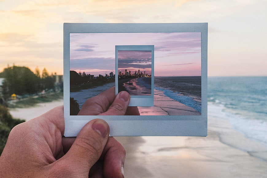 Hand holding polaroid photo of beach sunset cityscape