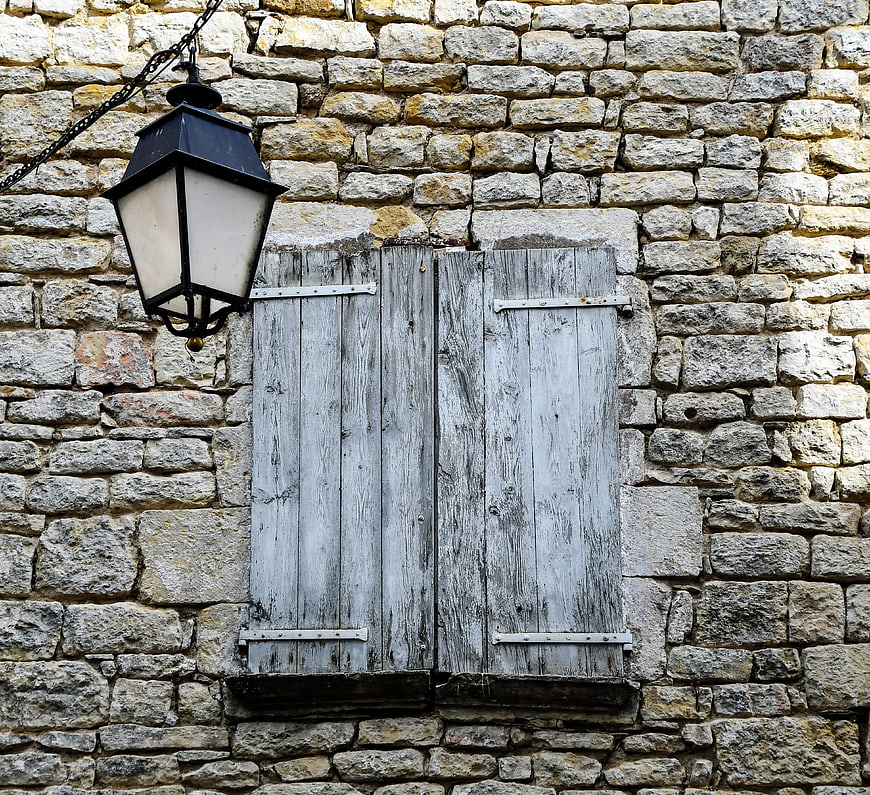 Rustic stone wall with weathered wooden shutters and lantern