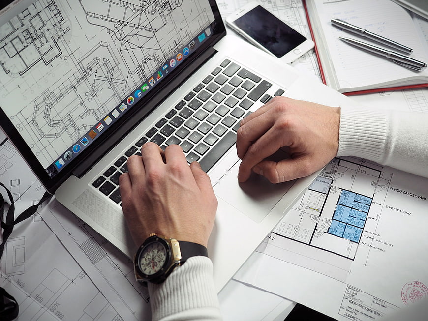 Architect working on laptop with blueprints and plans
