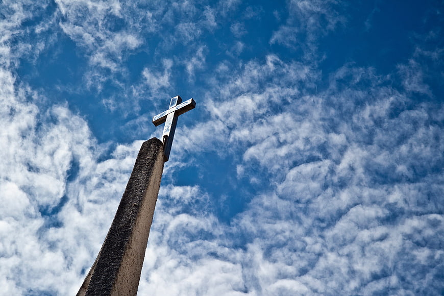 Christian Cross on Stone Pillar Against Blue Sky with Clouds