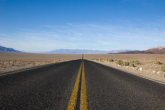 Endless desert highway stretching to distant mountains under blue sky
