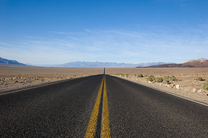 Endless desert highway stretching to distant mountains under blue sky