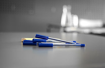 Blue pens and yellow sticky note on gray desk