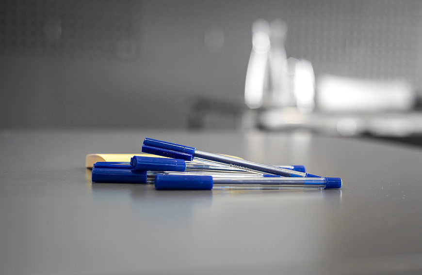 Blue pens and yellow sticky note on gray desk