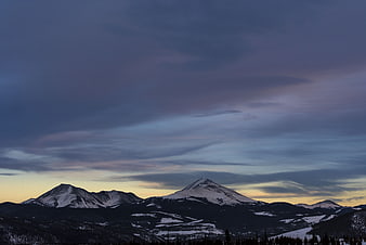 Snow-capped mountain peaks under dramatic twilight sky