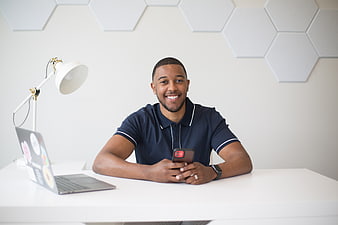Smiling Young Man at Desk with Smartphone and Laptop