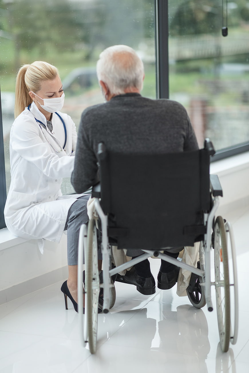 Doctor in Mask Talking to Senior Man in Wheelchair