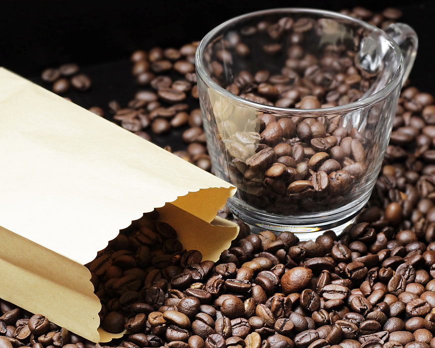 Roasted coffee beans in glass cup and paper bag on dark background
