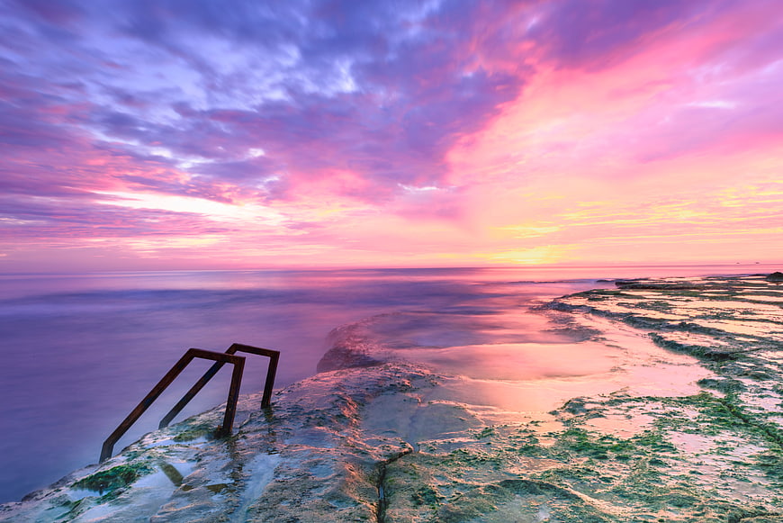 Vibrant Pink and Purple Sunset Over Rocky Ocean Coastline