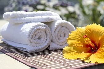 Rolled white towels and yellow hibiscus flower on bamboo mat