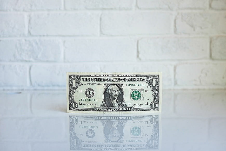 One Dollar Bill on White Brick Wall with Reflection
