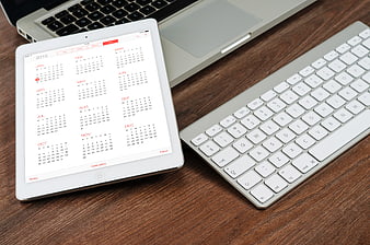White iPad Displaying 2015 Calendar Next To Apple Keyboard On Wooden Desk