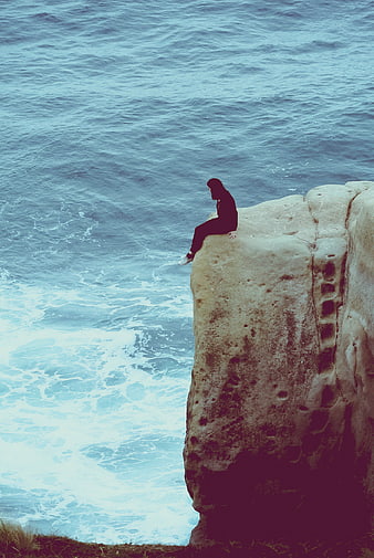 Person sitting on cliff edge overlooking ocean waves