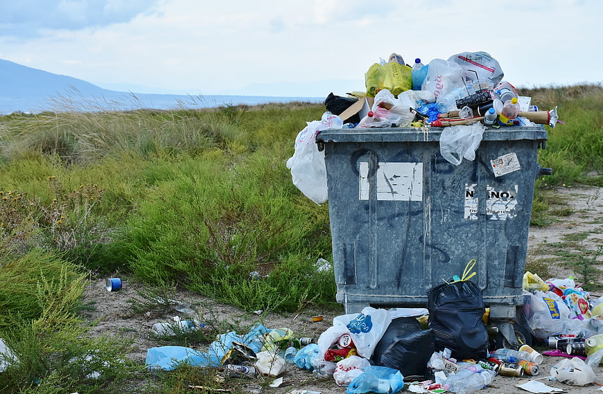 Overflowing dumpster with plastic waste in coastal dunes