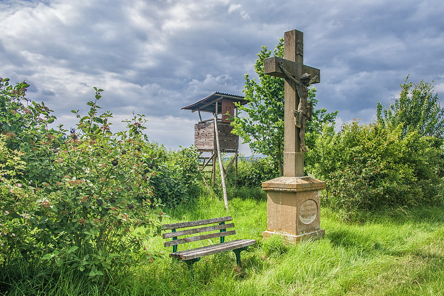 Rural landscape with crucifix, wooden bench, and hunting tower
