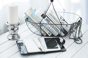 Wire basket with books, smartphone, and candle on white desk