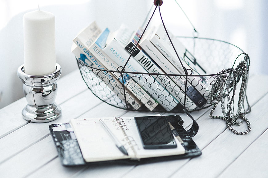Wire basket with books, smartphone, and candle on white desk